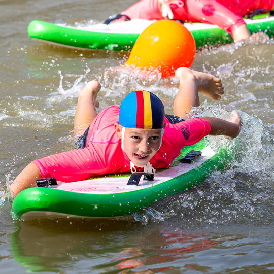  Young person on a surf board in water wearing a swim cap